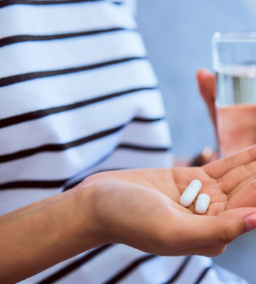 Hands of person in striped shirt holding 2 white pills and a glass of water