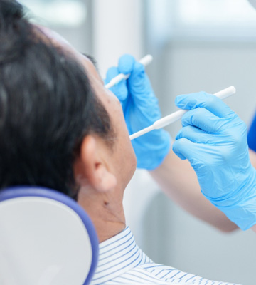 Dentist in blue scrubs and gloves performing a procedure on a patient