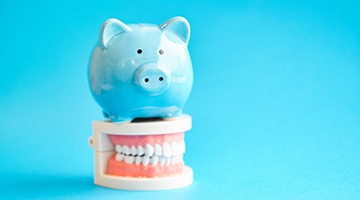 Piggy bank atop model teeth representing how to pay for dental emergencies in Colleyville