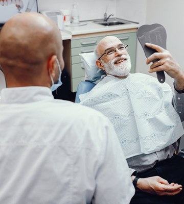 senior patient admiring his smile after getting dental implants in Colleyville