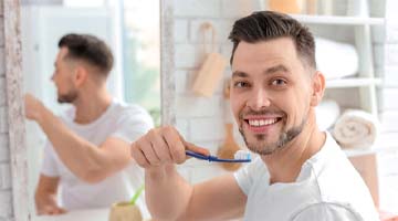 Man smiling while holding a toothbrush in a bathroom