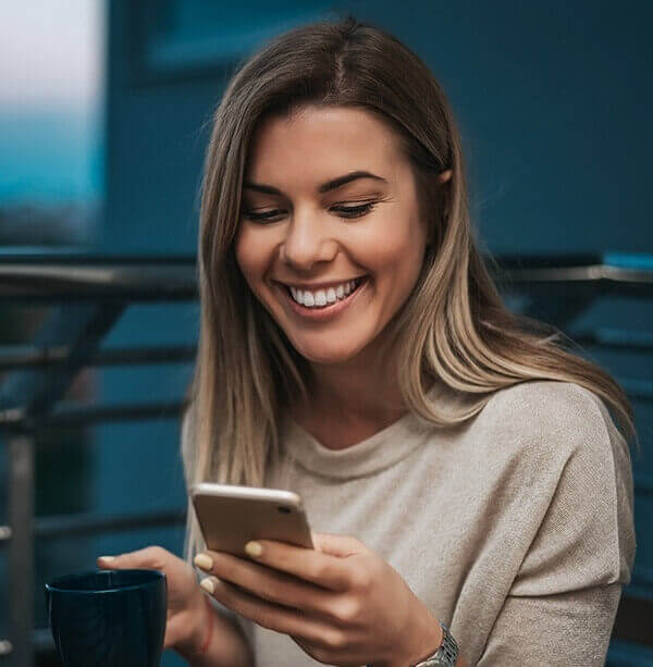 Young woman smiling at her phone while holding coffee mug