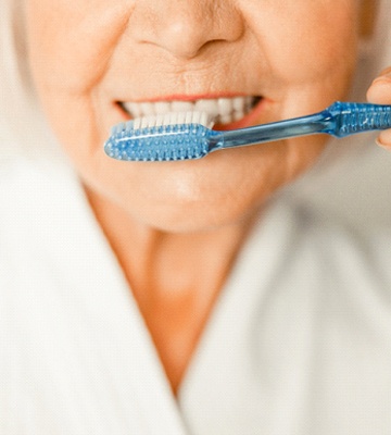 close-up of senior woman in white robe brushing teeth