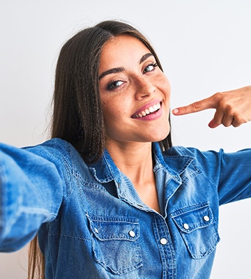 Woman in denim shirt smiling pointing to her teeth