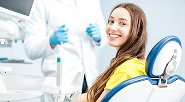 Woman smiling in dental chair wearing yellow shirt looking back at camera