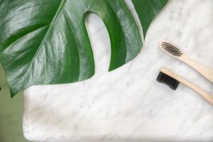 Two bamboo toothbrushes next to a large leaf on a marble surface