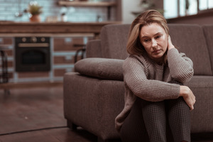 Woman sitting in front of her couch looking depressed